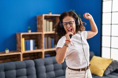 Orta yaşlı İspanyol kadın evde kulaklık takarak dans ediyor.