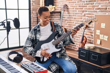 Afrikalı Amerikalı kadın müzisyen, müzik stüdyosunda elektro gitar çalarken gülümsüyor.