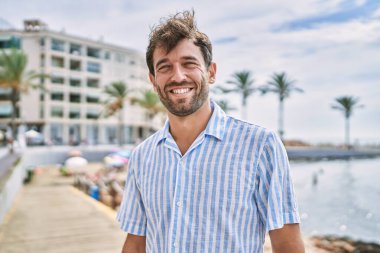 Genç İspanyol gülümseyen adam sahilde mutlu bir şekilde duruyor..