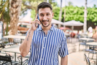 Genç yakışıklı adam parkta telefonla konuşuyor.