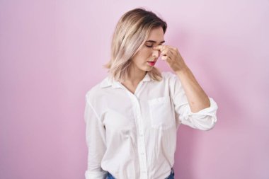 Pembe arka planda duran genç ve güzel bir kadın yorgun burnu ve gözleri ovuşturuyor yorgunluk ve baş ağrısı hissediyor. Stres ve hüsran kavramı. 