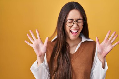 Sarı arka planda duran genç esmer kadın başarı için deli ve deli olan gözlüklerini takıyor kollarını kaldırmış ve gözlerini kapatmış heyecanla haykırıyor. Kazanan konsept 