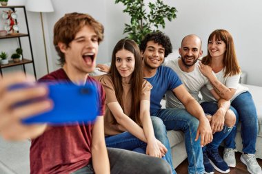 Group of young friends smiling happy make selfie by the smartphone sitting on the sofa at home.