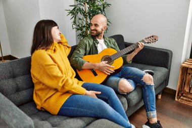 Genç İspanyol çift gülümseyerek evde kanepede oturmuş klasik gitar çalıyor..