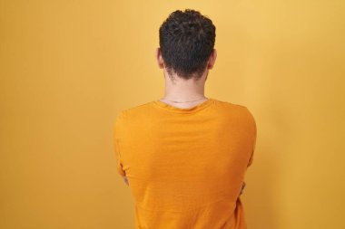 Sarı arka planda dikilen İspanyol genç adam çapraz kollarla diğer tarafa bakıyor. 