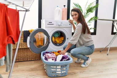 Young hispanic woman smiling confident washing clothes at laundry room