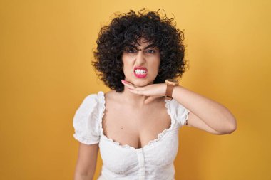 Sarı arka planda duran kıvırcık saçlı genç esmer kadın bıçakla boğazını kesiyor, saldırganlığı şiddetli bir şiddetle tehdit ediyor. 
