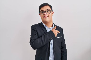 Down sendromlu genç İspanyol bir adam iş stili giyiniyor. Neşeli. Yüzünde mutlu ve doğal bir ifadeyle elleri ve parmaklarıyla yüzünü gösteren bir gülümseme var. 