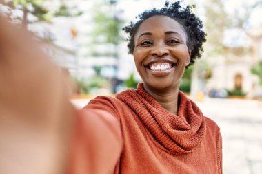 Gülümseyen Afrikalı Amerikalı genç kız şehirdeki akıllı telefondan selfie çekiyor..