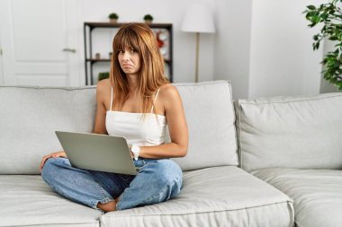 İspanyol kadın evdeki kanepede oturmuş dizüstü bilgisayar kullanıyor. Depresyonda ve endişe içinde, sinirli ve korkmuş bir şekilde ağlıyor. hüzünlü ifade. 