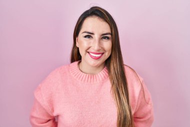 Yüzünde mutlu ve havalı bir gülümsemeyle pembe arka planda duran genç İspanyol kadın. şanslı kişi. 