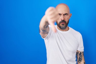 Mavi arka planda duran İspanyol dövmeli adam mutsuz ve kızgın görünüyor. Reddedilmiş ve olumsuz. kötü ifade. 