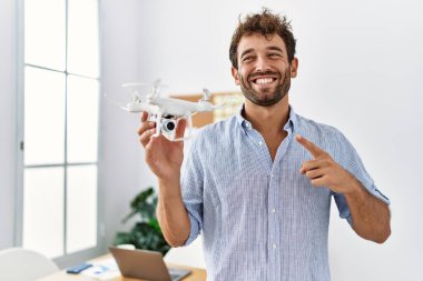 Mimarlık ofisinde İHA kullanan genç yakışıklı adam mutlu bir şekilde el ve parmak işareti yapıyor. 
