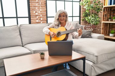 Orta yaşlı bir kadının evde online gitar dersi var.