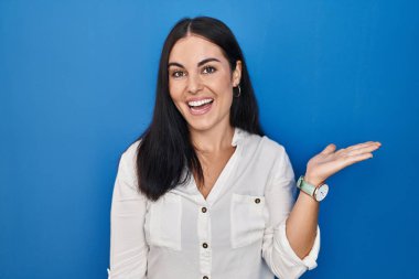 Mavi arka planda dikilen genç İspanyol kadın mutlu bir şekilde sunum yapıyor ve avuç içi kameraya bakıyor.. 