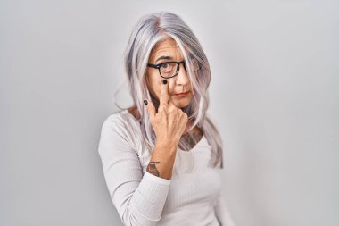 Beyaz arka planda gri saçlı orta yaşlı bir kadın. Gözünü dikip jestini izliyor. Şüpheli bir ifade. 
