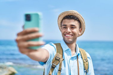 Afro-Amerikalı turist gülümseyip, deniz kenarındaki akıllı telefondan selfie çekiyor.