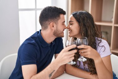 Young hispanic couple drinking wine sitting on table at home