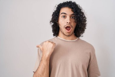 Beyaz arka planda duran kıvırcık saçlı İspanyol adam elleri yana dönük, ağzı açık şaşkın bir ifadeyle şaşırdı.. 