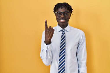 Sarı arka planda dikilen Afrikalı adam bir numarayı gösterip işaret ederken kendinden emin ve mutlu gülümsüyor.. 