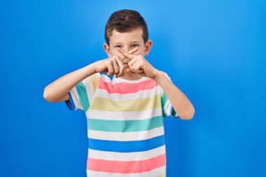 Genç beyaz çocuk mavi arka planda duruyor. Reddedilme ifadesi negatif işaret veriyor. 