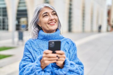 Middle age grey-haired woman smiling confident using smartphone at street