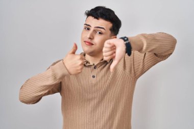 Non binary person standing over isolated background doing thumbs up and down, disagreement and agreement expression. crazy conflict 