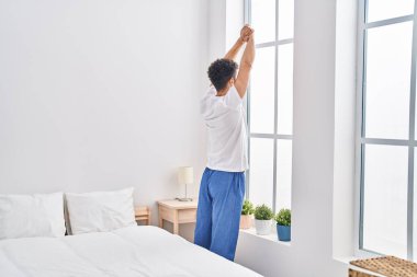 Young arab man waking up stretching arms at bedroom