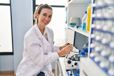 Young woman wearing scientist uniform using microscope at laboratory
