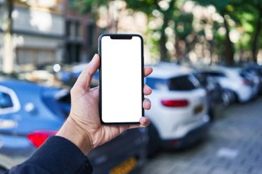 Akıllı telefon tutan adam araba parkında beyaz boş ekran gösteriyor.