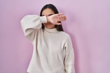 Pembe arka planda duran genç Güney Asyalı kadın kollarıyla gözlerini kapatıyor, ciddi ve üzgün görünüyor. Görme, saklama ve reddetme konsepti 