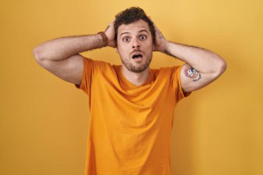 Sarı arka planda dikilen İspanyol genç adam deli ve elleri başının üstünde korkmuş, korkmuş ve ağzı açık şoktan şaşırmış. 