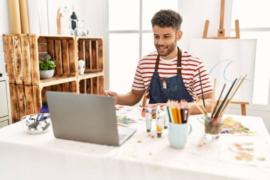 Sanat stüdyosunda dizüstü bilgisayar kullanan genç bir Arap sanatçı..