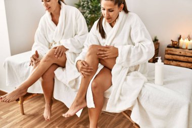 İki kadın bornoz giyip masaj yapıyorlar. Güzellik merkezinde krem sürüyorlar.