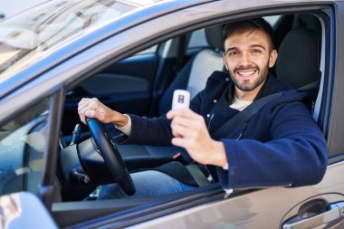 Young hispanic man smiling confident holding key of new car at street