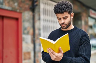 Sokakta kitap okuyan rahat ifadeli genç bir Arap.