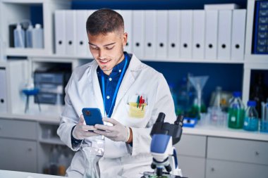 Young hispanic man scientist using smartphone at laboratory