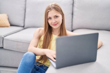 Young caucasian woman using laptop sitting on floor at home