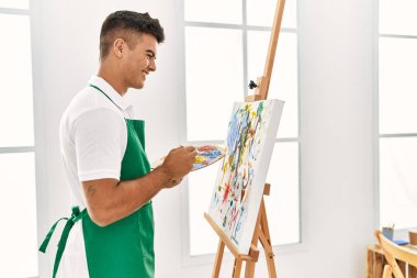 Genç İspanyol adam resim stüdyosunda kendine güvenen gülümsüyor.