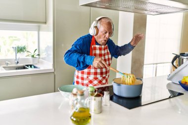 Senior man listening to music cooking spaghetti at kitchen