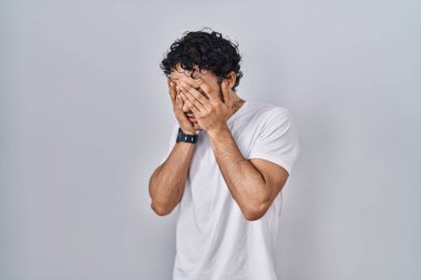 Hispanik bir adam izole edilmiş arka planda duruyor. Ağlarken suratını ellerle kapatıyor. depresyon kavramı. 