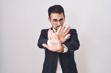 Handsome business hispanic man standing over white background rejection expression crossing arms and palms doing negative sign, angry face 