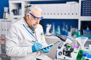 Middle age grey-haired man scientist writing report working at laboratory