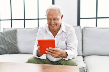 Kıdemli adam evde dokunmatik ped kullanarak kendinden emin bir şekilde gülümsüyor.