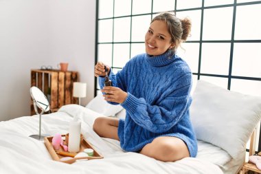 Genç, güzel, İspanyol bir kadın. Yatak odasında cilt losyonu sürüyor.