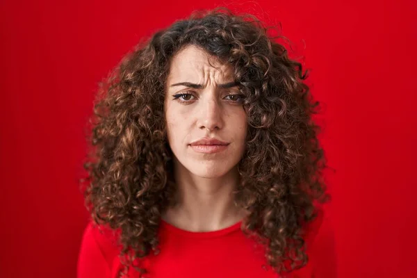 Kırmızı Arka Planda Dikilen Kıvırcık Saçlı Spanyol Kadın Depresif Endişeli — Stok fotoğraf