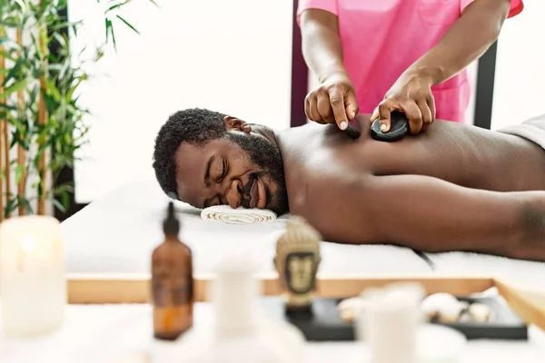 African american man reciving back massage with black stones at beauty center.