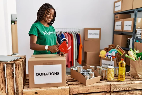 在慈善中心身穿志愿制服包装捐赠箱的年轻非洲裔美国妇女 — 图库照片