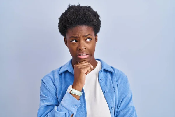 African american woman standing over blue background thinking worried about a question, concerned and nervous with hand on chin