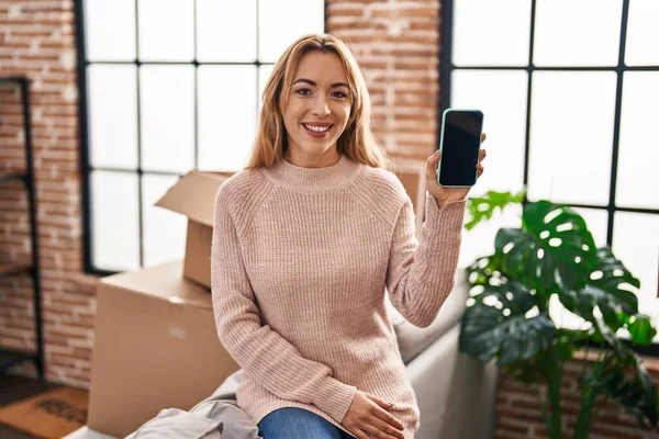 スマートフォンの画面を示す新しい家に移動するヒスパニック系の女性ポジティブで幸せな立っていると歯を示す自信を持って笑顔で笑顔 — ストック写真